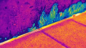A thermal imaging camera showing a heat map of a wall or floor locating moisture.